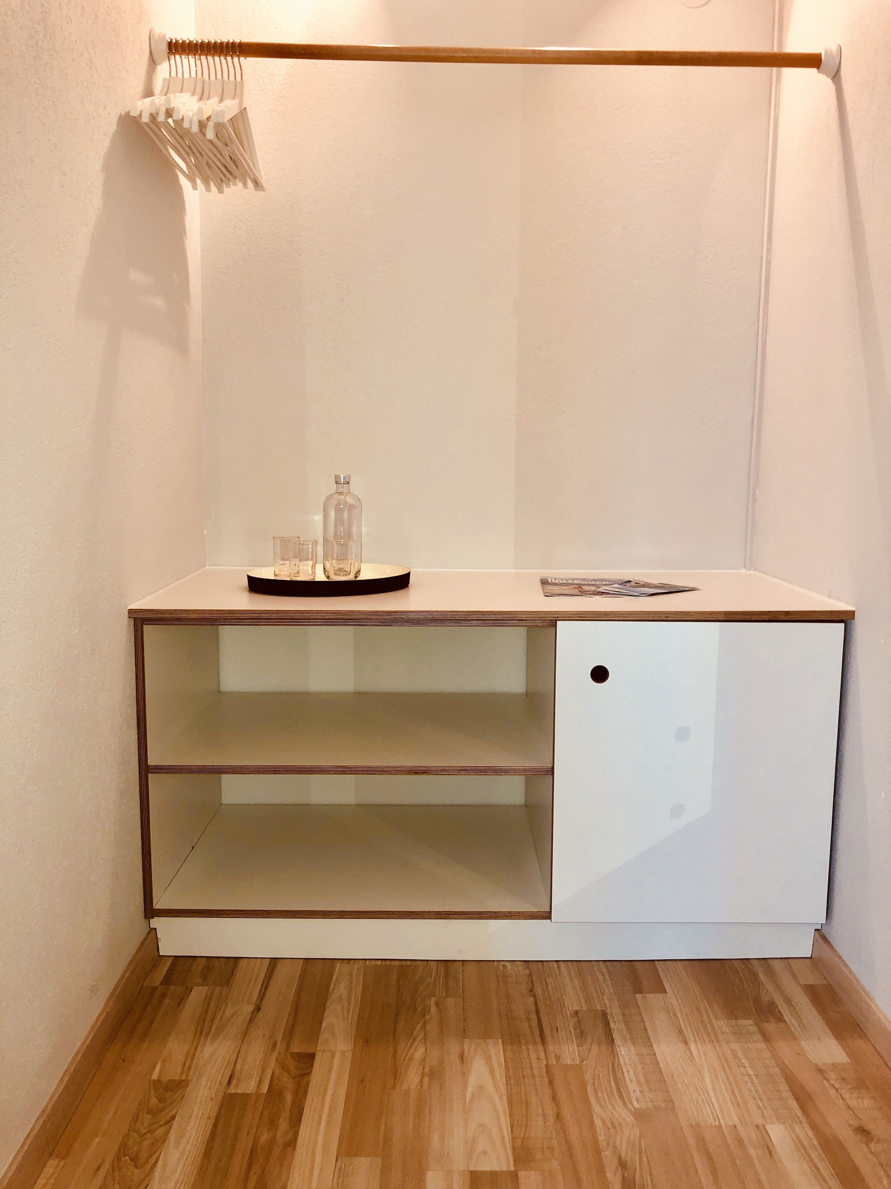 Un meuble blanc avec deux étagères et un seul tiroir, un plancher en bois et un porte-serviettes fixé au mur.