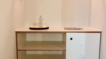 Un meuble blanc avec deux étagères et un seul tiroir, un plancher en bois et un porte-serviettes fixé au mur.