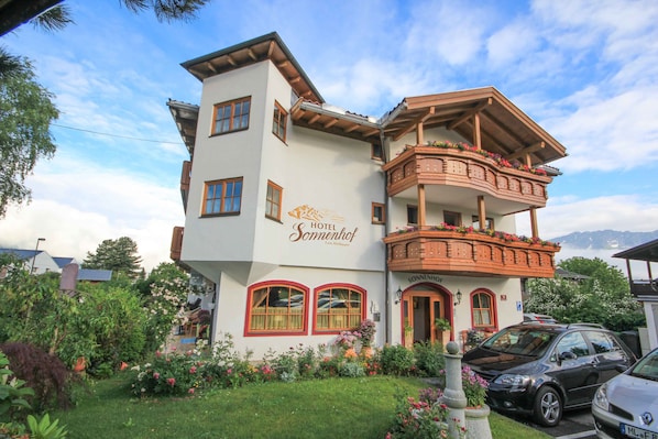 A two-story hotel with a balcony on the upper floor, surrounded by a well-maintained garden.