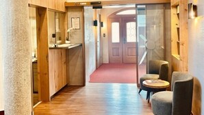 A hallway with wooden flooring, a reception desk, a seating area with two chairs, and a staircase. - Hotel Sonnenhof - bed & breakfast & appartements (Innsbruck)
