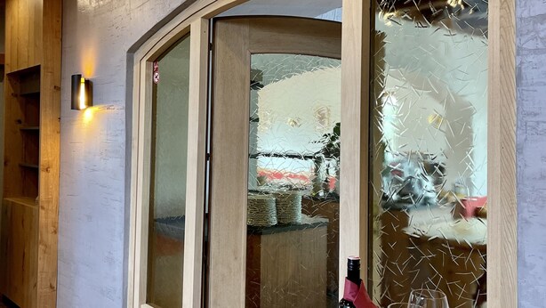 A room with wooden flooring, a curved wooden door, a table with a bottle and glasses, and a wall-mounted light. - Hotel Sonnenhof - bed & breakfast & appartements (Innsbruck)