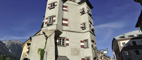 Un edificio de varios pisos con contraventanas rojas y blancas, una placa y una estatua en su fachada.