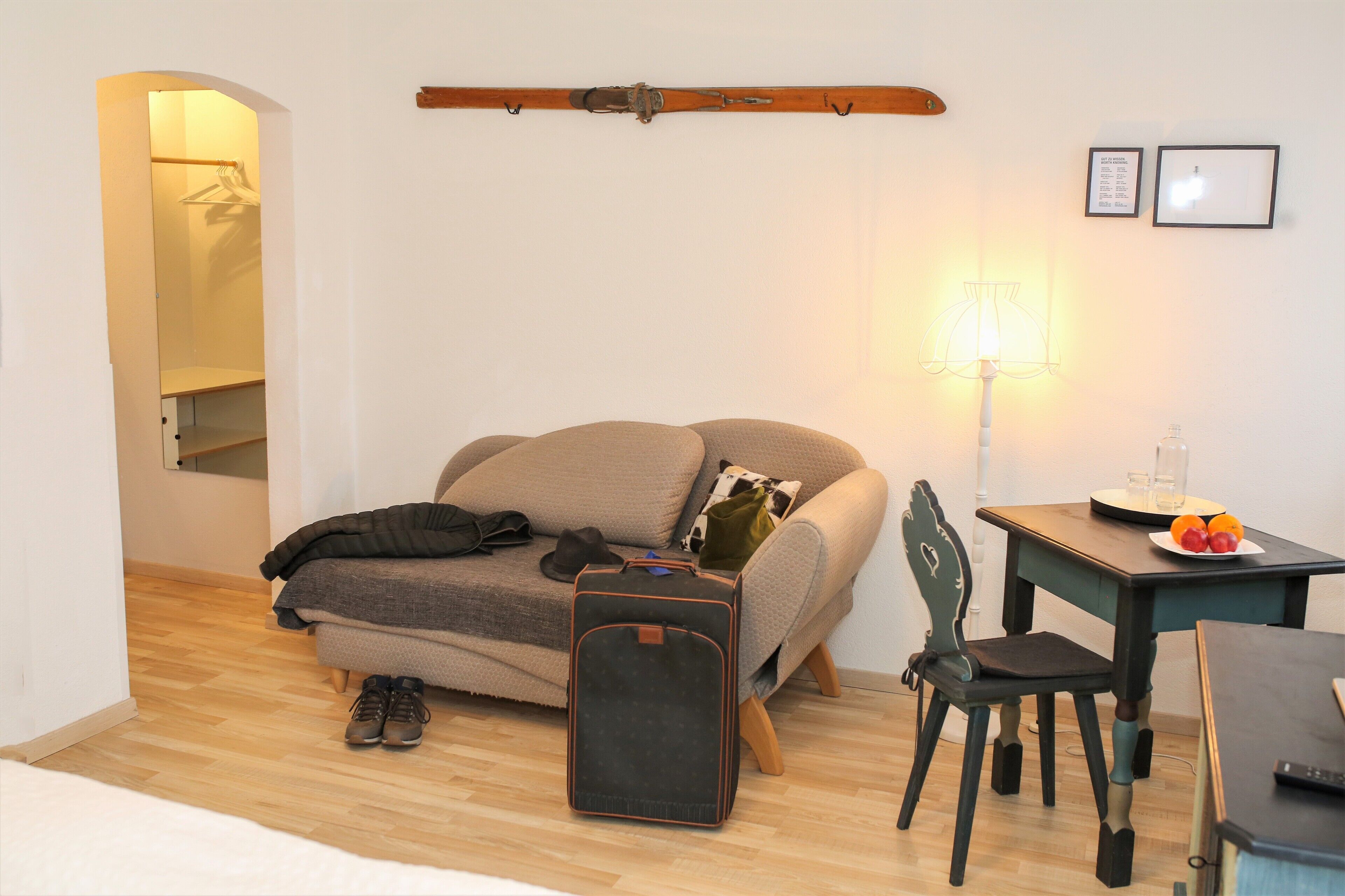 A cozy room with a sofa, a small table with a plate of fruit, a chair, a suitcase, and a lamp.