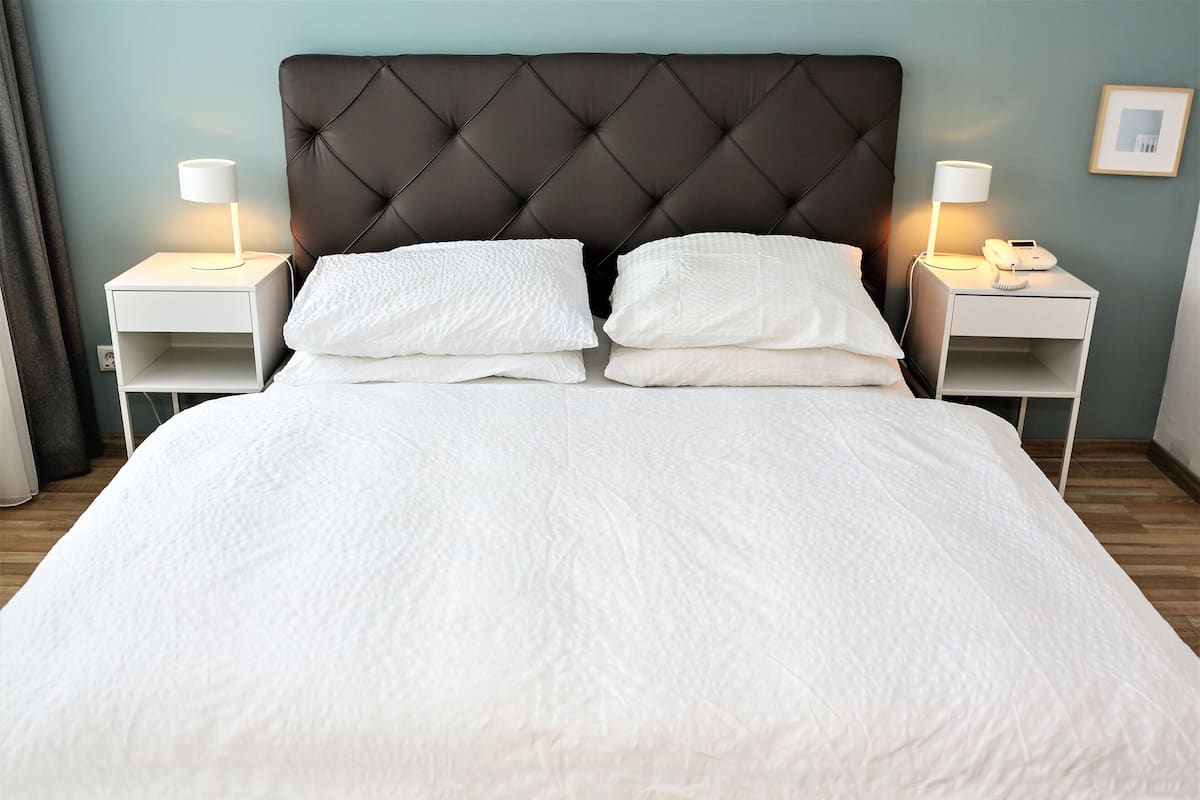 A neatly made bed with white linens, two bedside tables with lamps, and a dark tufted headboard.