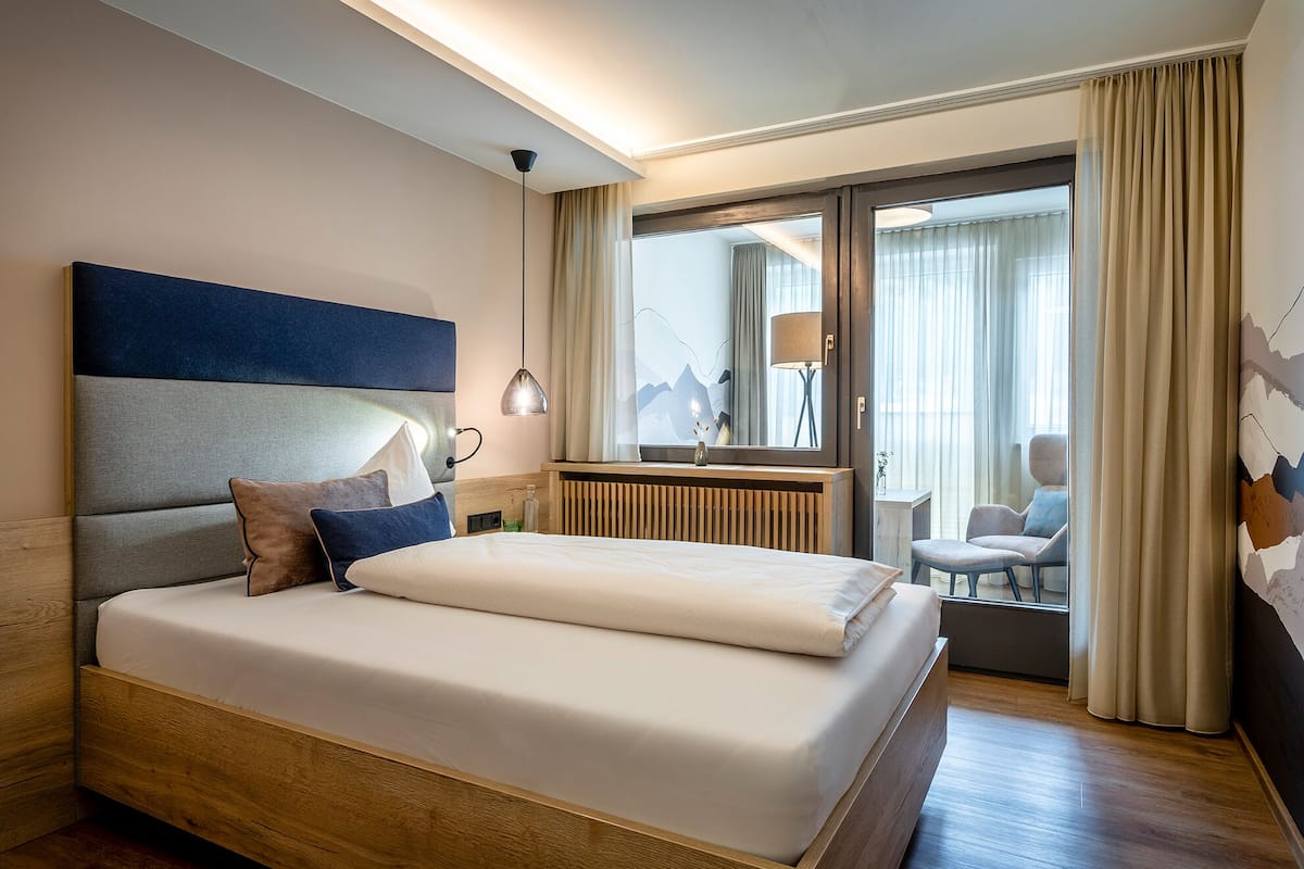 Una habitación de hotel moderna con una cama grande, un escritorio, una silla y vistas de la ciudad a través de la ventana.