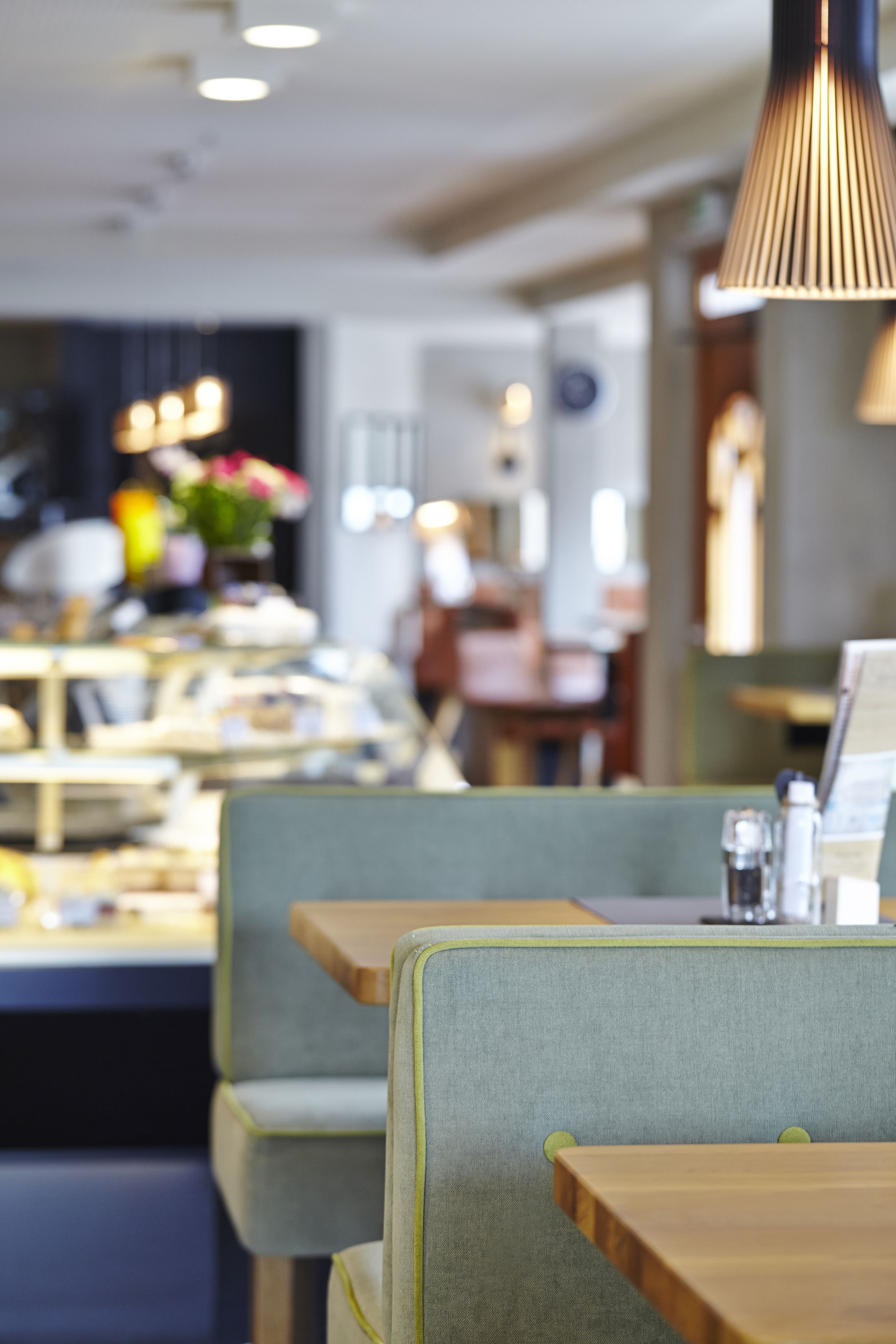 En restaurantindretning med grønne polstrede bænke, træborde og hængende lamper.