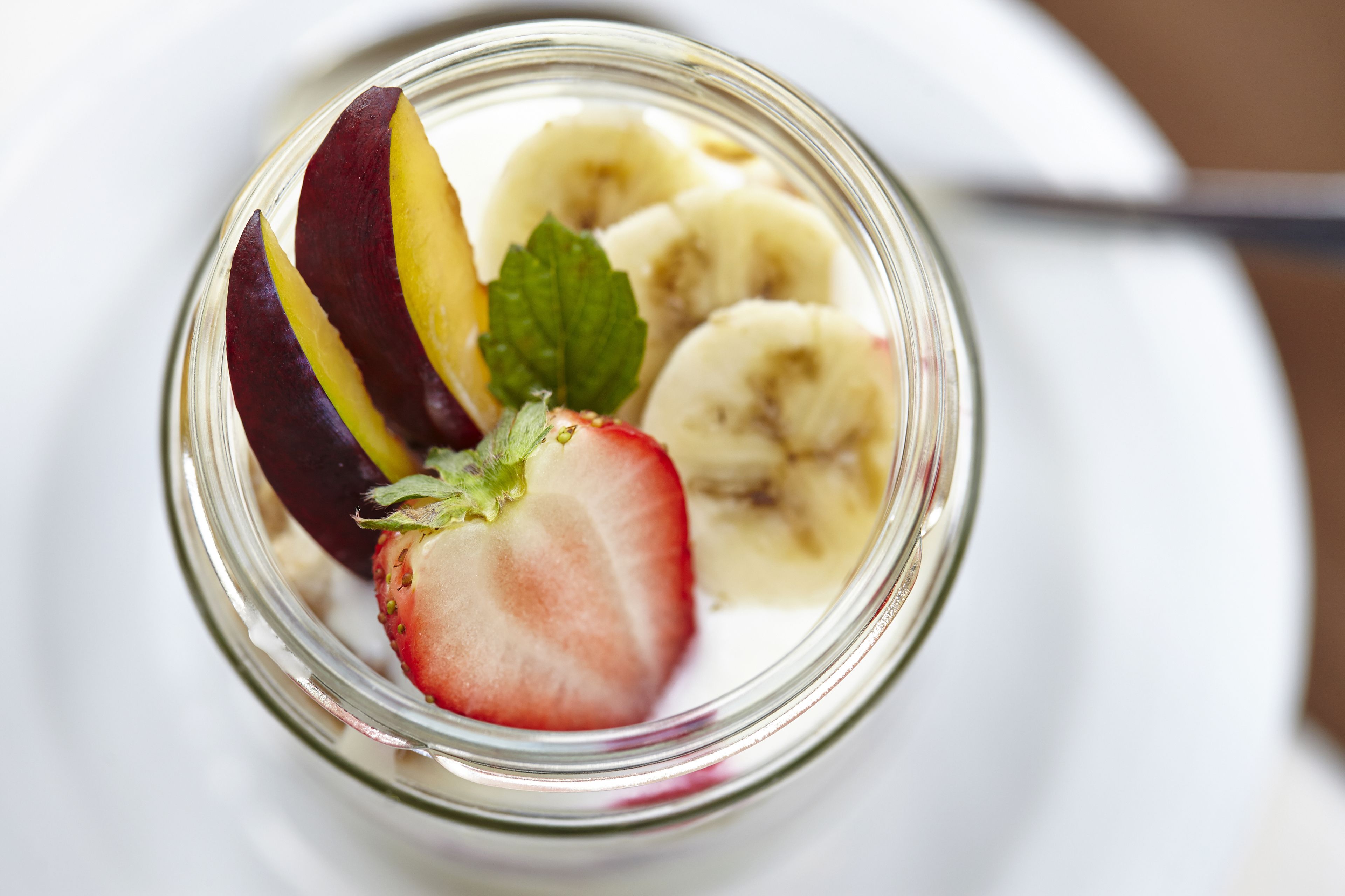 A clear glass jar containing sliced fruits and a strawberry.