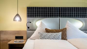 A neatly made bed with white and patterned pillows, a wooden nightstand with a magazine, and a wall-mounted lamp.