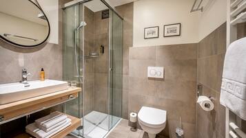Un baño moderno con ducha envuelta en vidrio, un lavamanos blanco con mueble de madera y un inodoro con perchero.