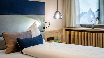 Une chambre d’hôtel avec un lit, une table de chevet, une lampe, une fenêtre donnant sur les montagnes et un radiateur.