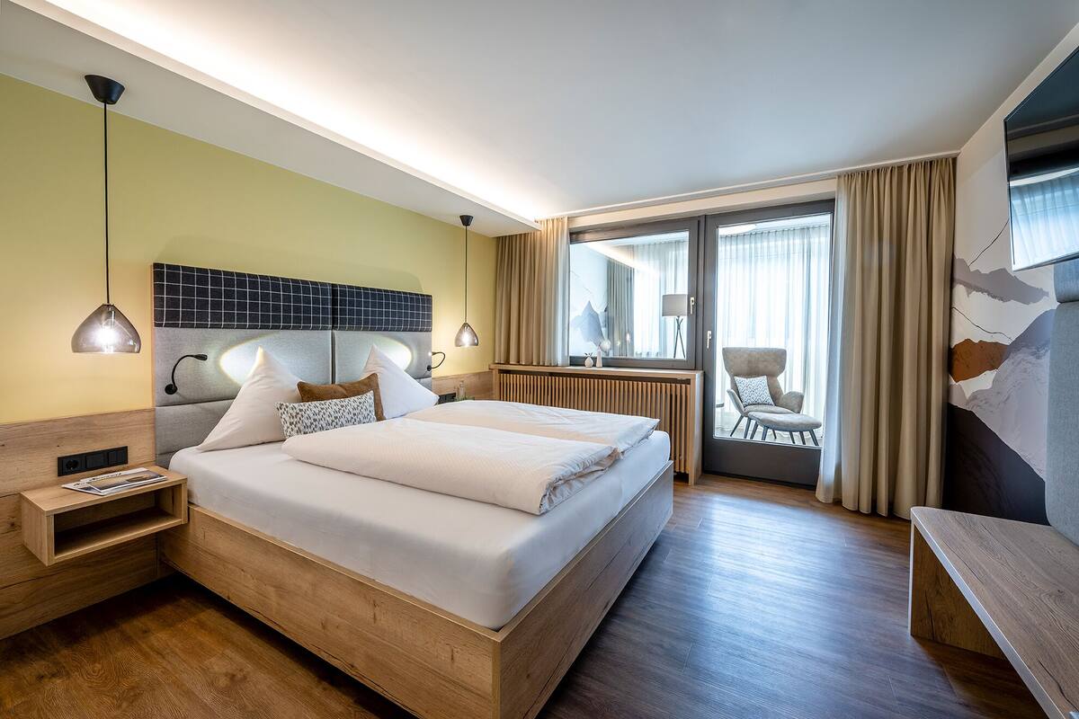 Una habitación de hotel con una cama grande, mesitas de noche, un escritorio y vistas al exterior.