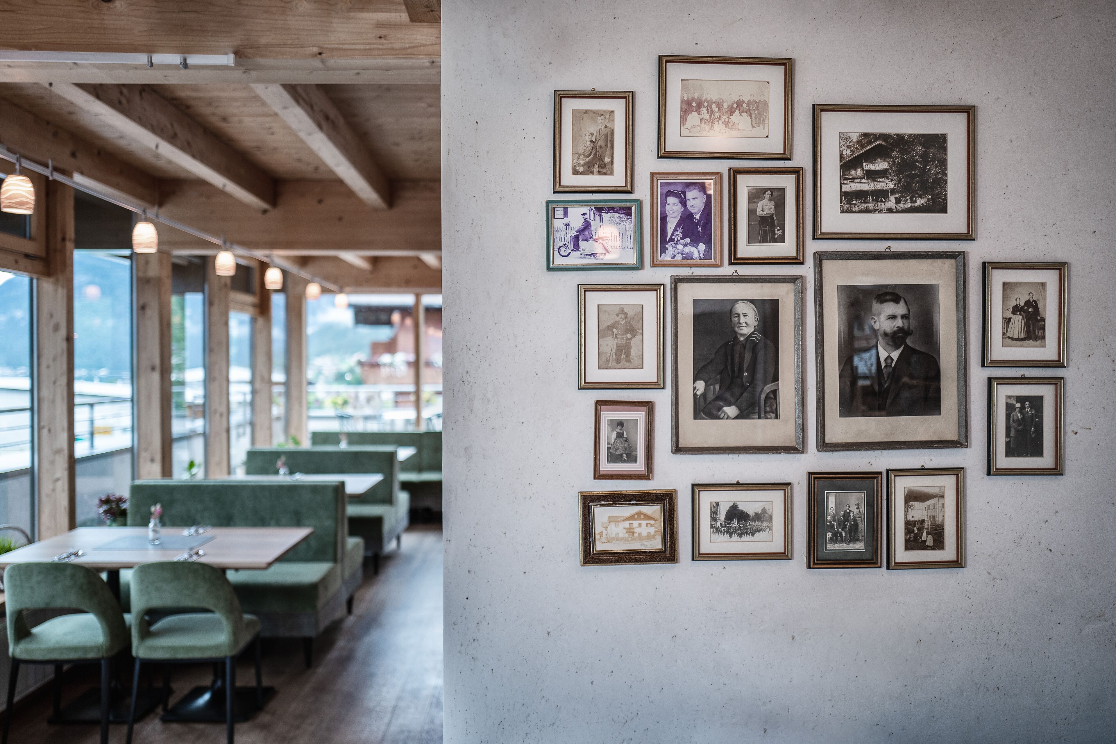 A restaurant with wooden beams, green upholstered booths, and a wall of framed black and white photographs.
