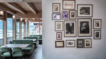 A restaurant with wooden beams, green upholstered booths, and a wall of framed black and white photographs.
