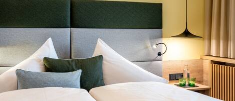 Habitación de hotel con una cama grande, cabecero con diseño geométrico, mesita de noche con vasos y una lámpara.
