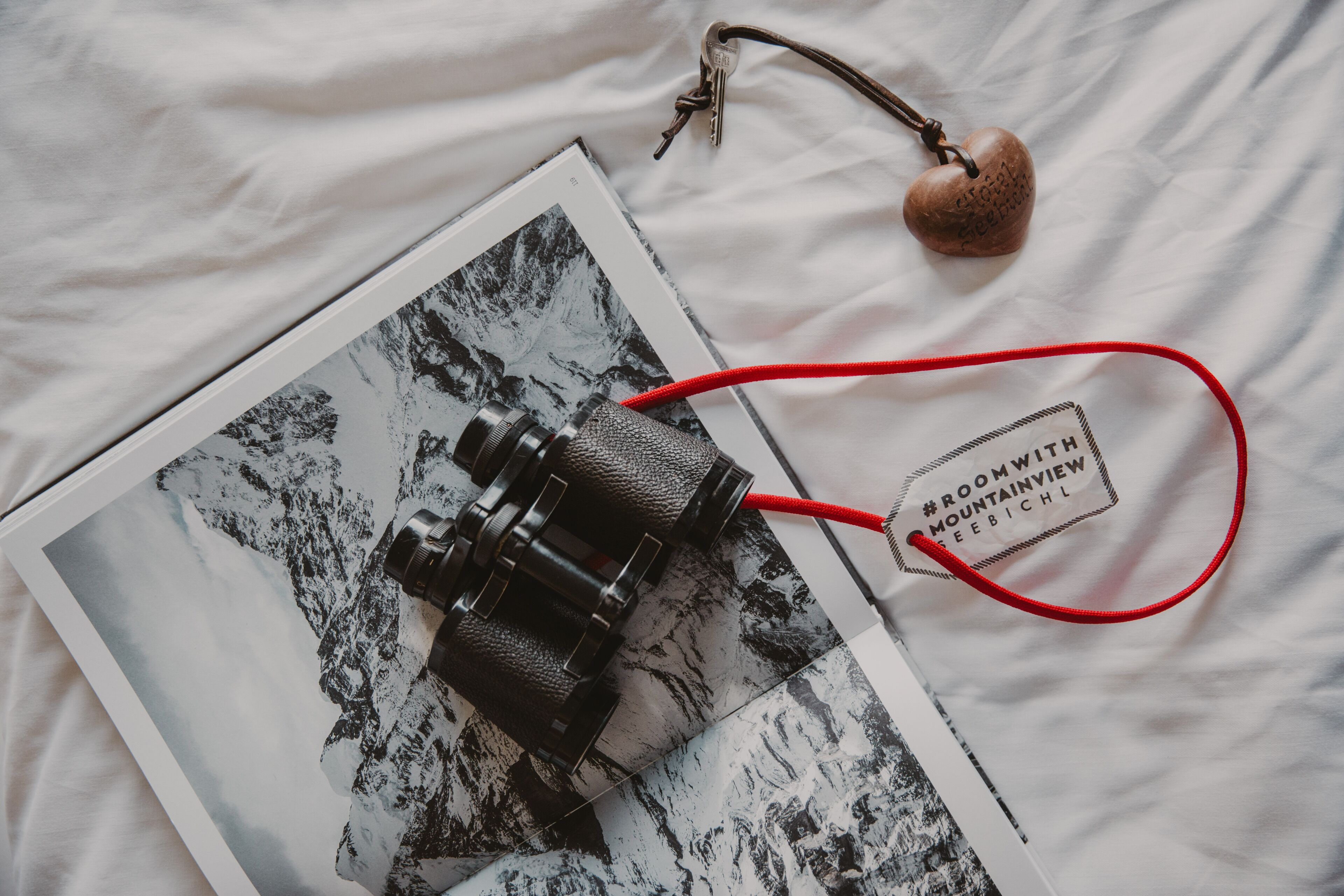 A camera on a bed with a book and a heart-shaped keychain.