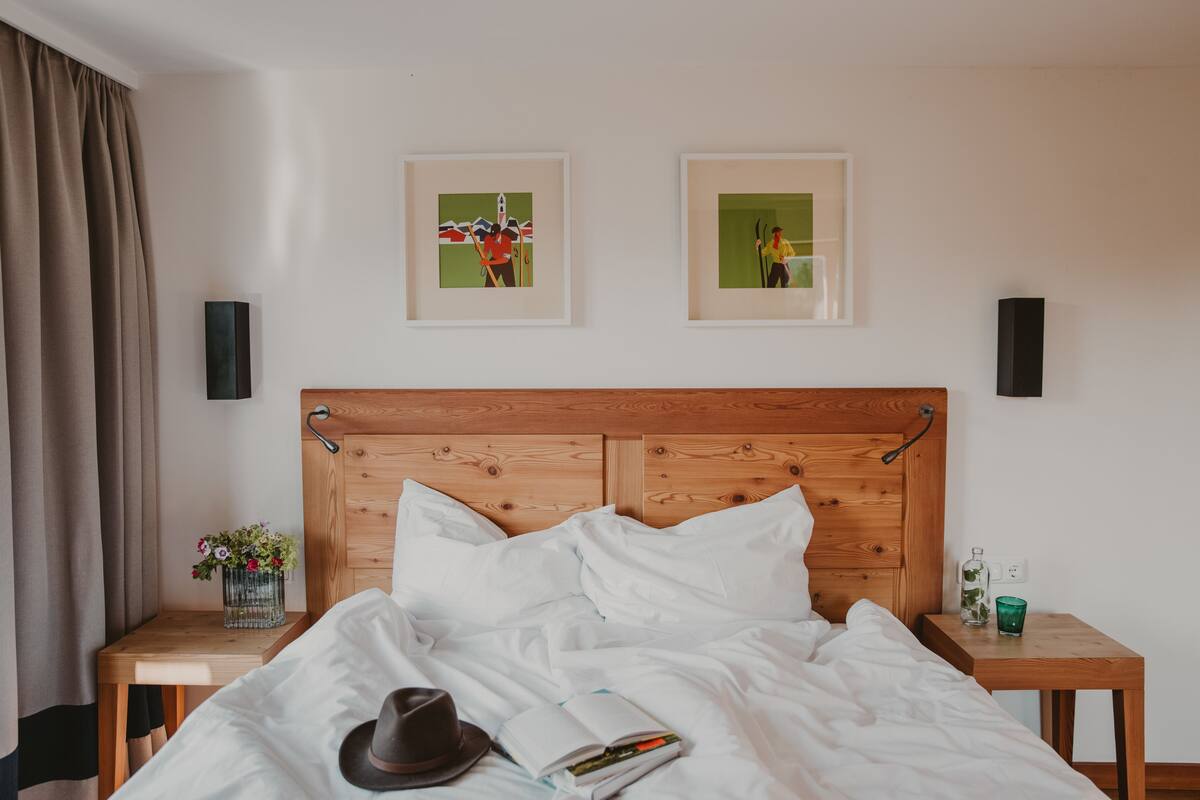 Una cama bien hecha con sábanas blancas, un cabecero de madera y dos cuadros enmarcados en la pared.