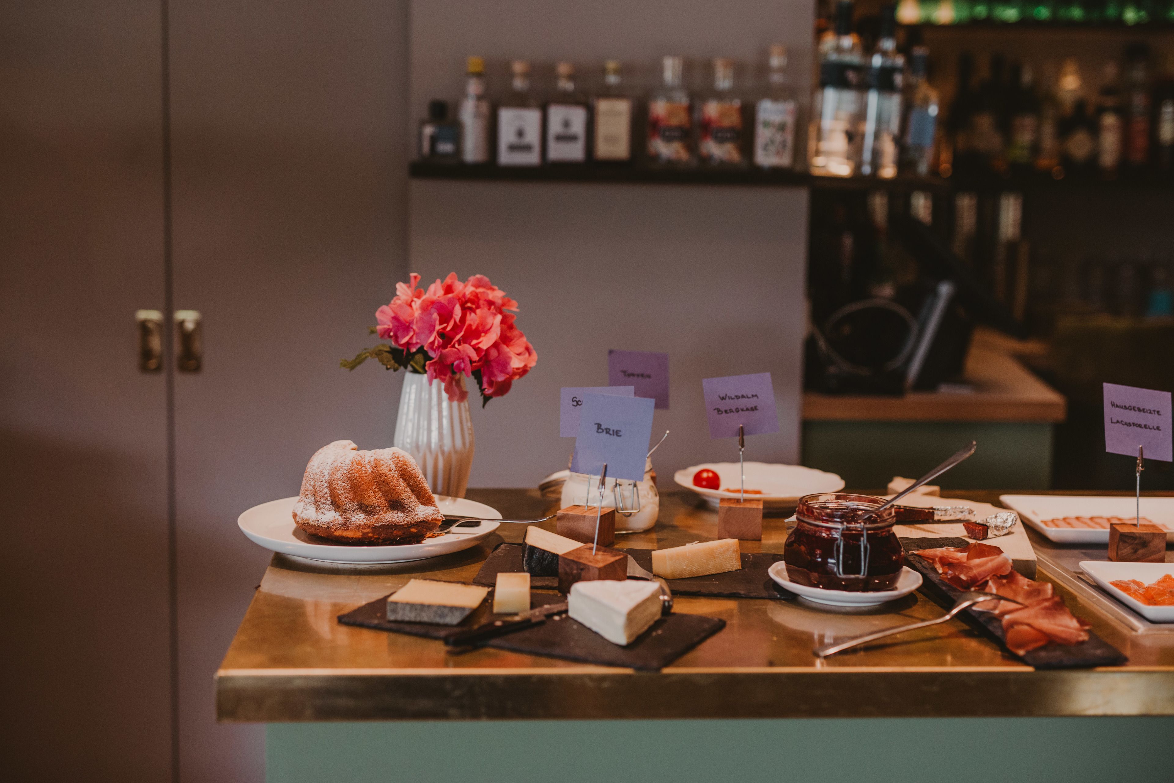 Una mesa de buffet con varios quesos, un pastel Bundt y un jarrón de flores.