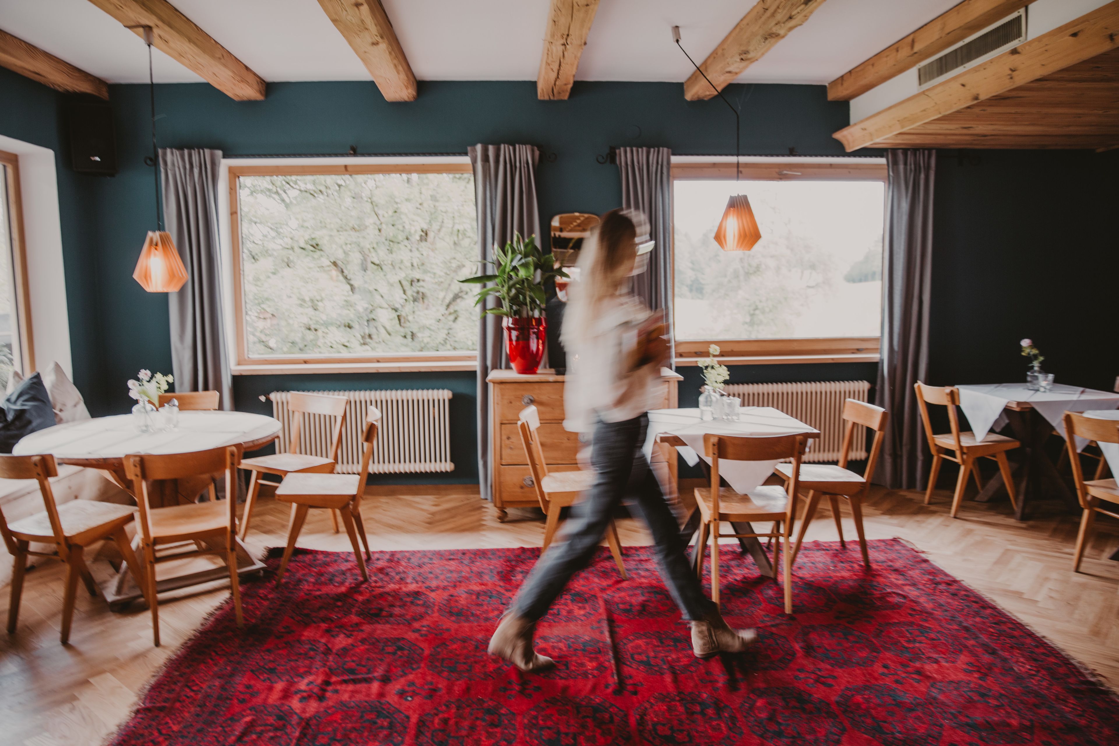 Un comedor con mobiliario de madera, ventanas amplias y un tapete rojo estampado.