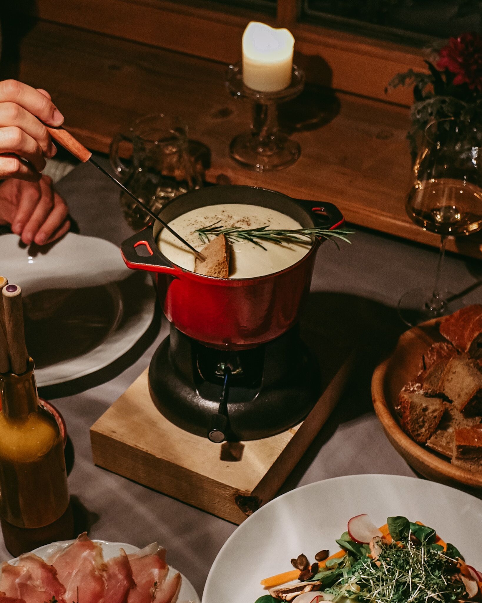 A dining table with a red pot of soup, a candle, and various dishes including a plate of meat and a salad.