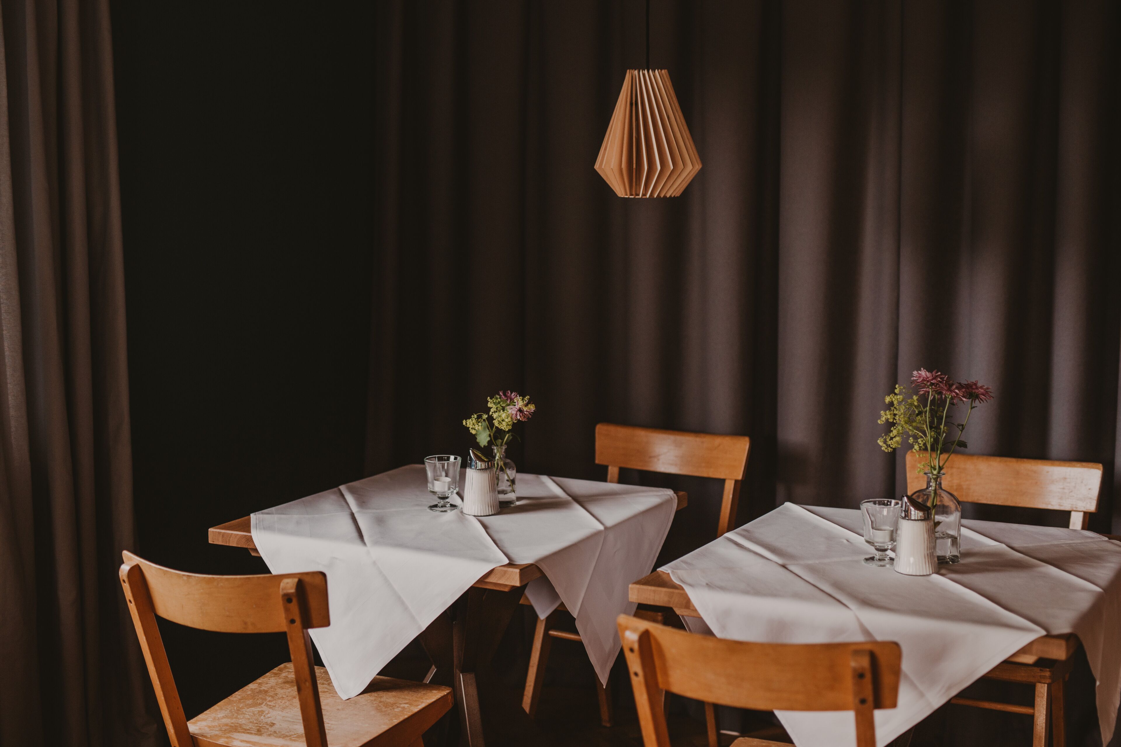 A dining table set with white tablecloths, wooden chairs, and small vases with flowers.