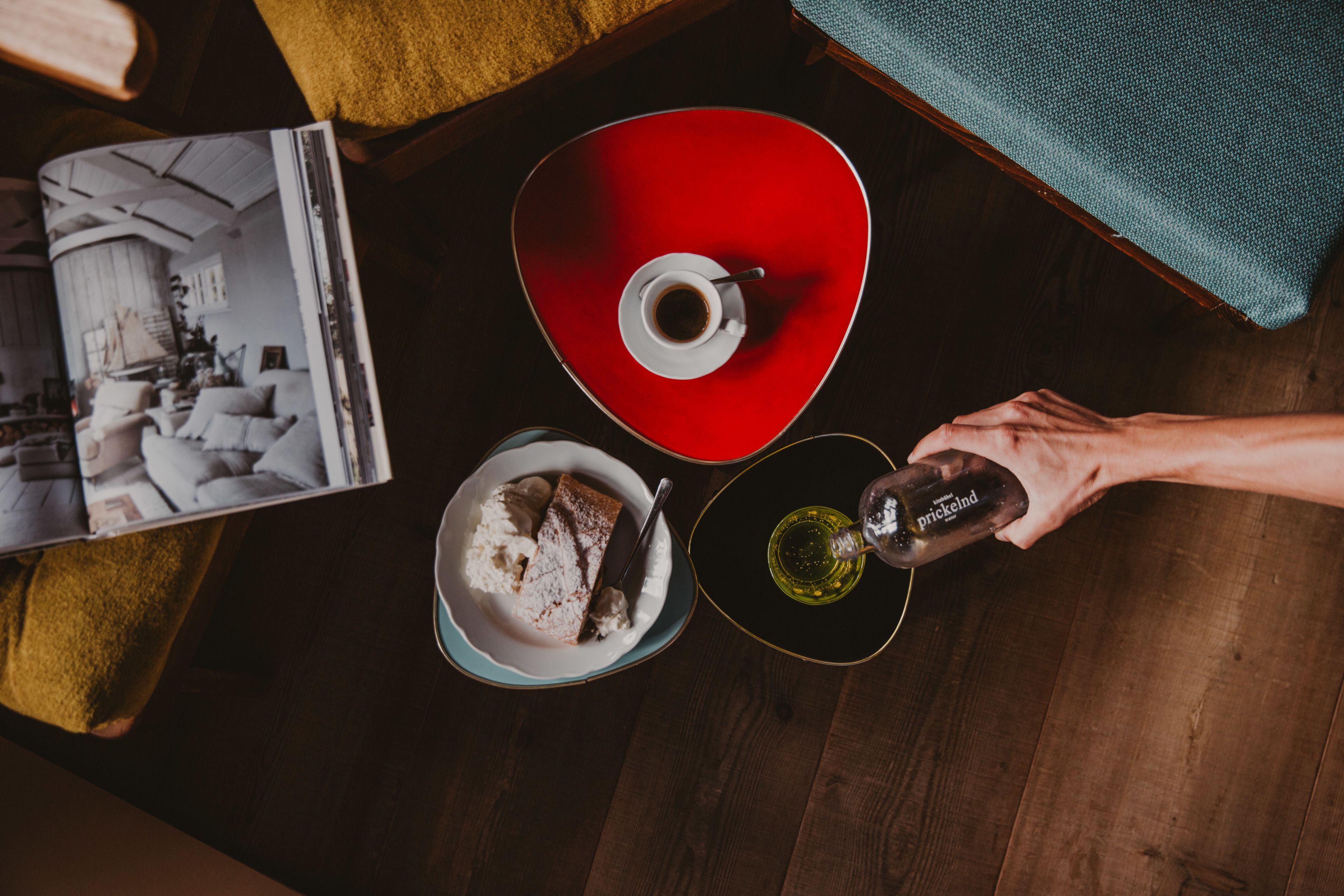 A top-down view of a table with a red bowl, a white plate with a dessert, and a bottle of Prickind.
