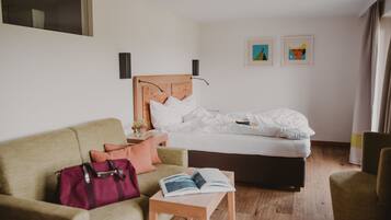 A hotel room with a bed, a sofa, a table with a book, a bag, and two framed pictures on the wall.