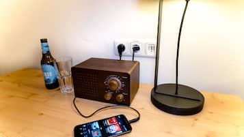 Uma mesa de madeira com uma garrafa, um copo, um rádio e um smartphone.