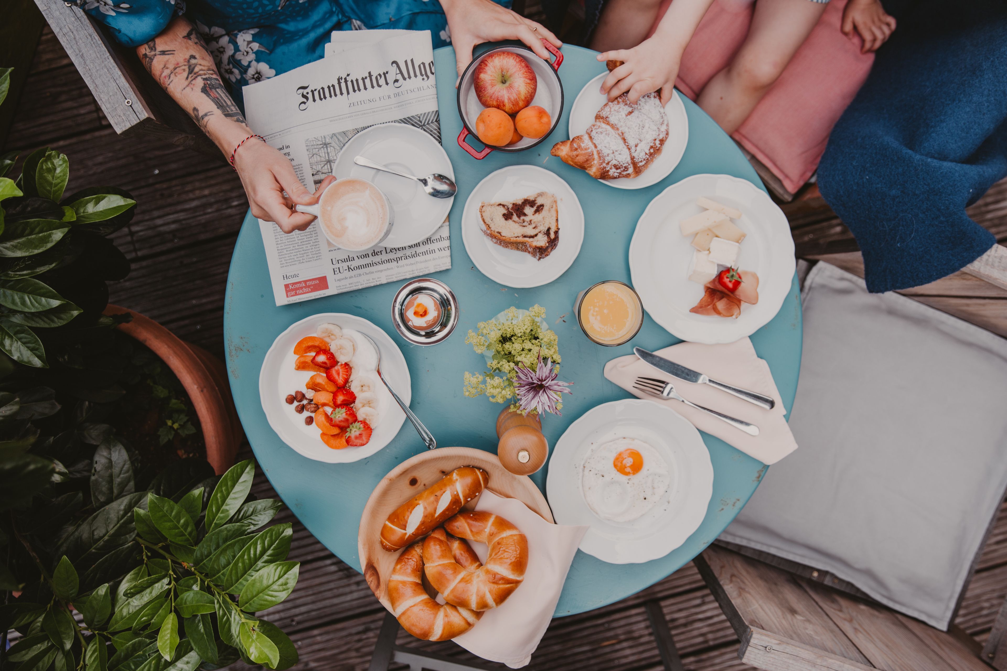 A round table with various breakfast items, including pastries, fruits, and a newspaper.