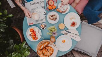 A round table with various breakfast items, including pastries, fruits, and a newspaper.