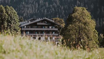 A two-story building with a sloped roof, surrounded by trees and a mountainous backdrop.