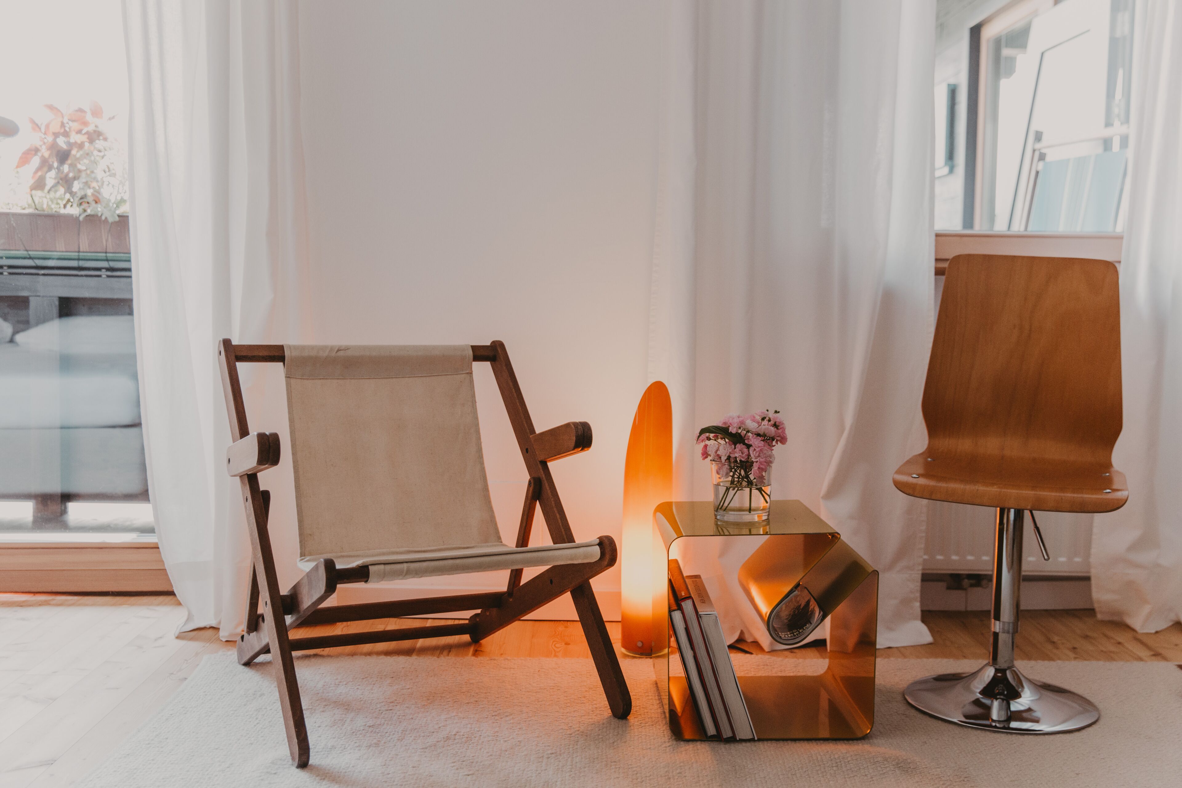 A room with a wooden chair, a small table with a vase of flowers, and a lamp.