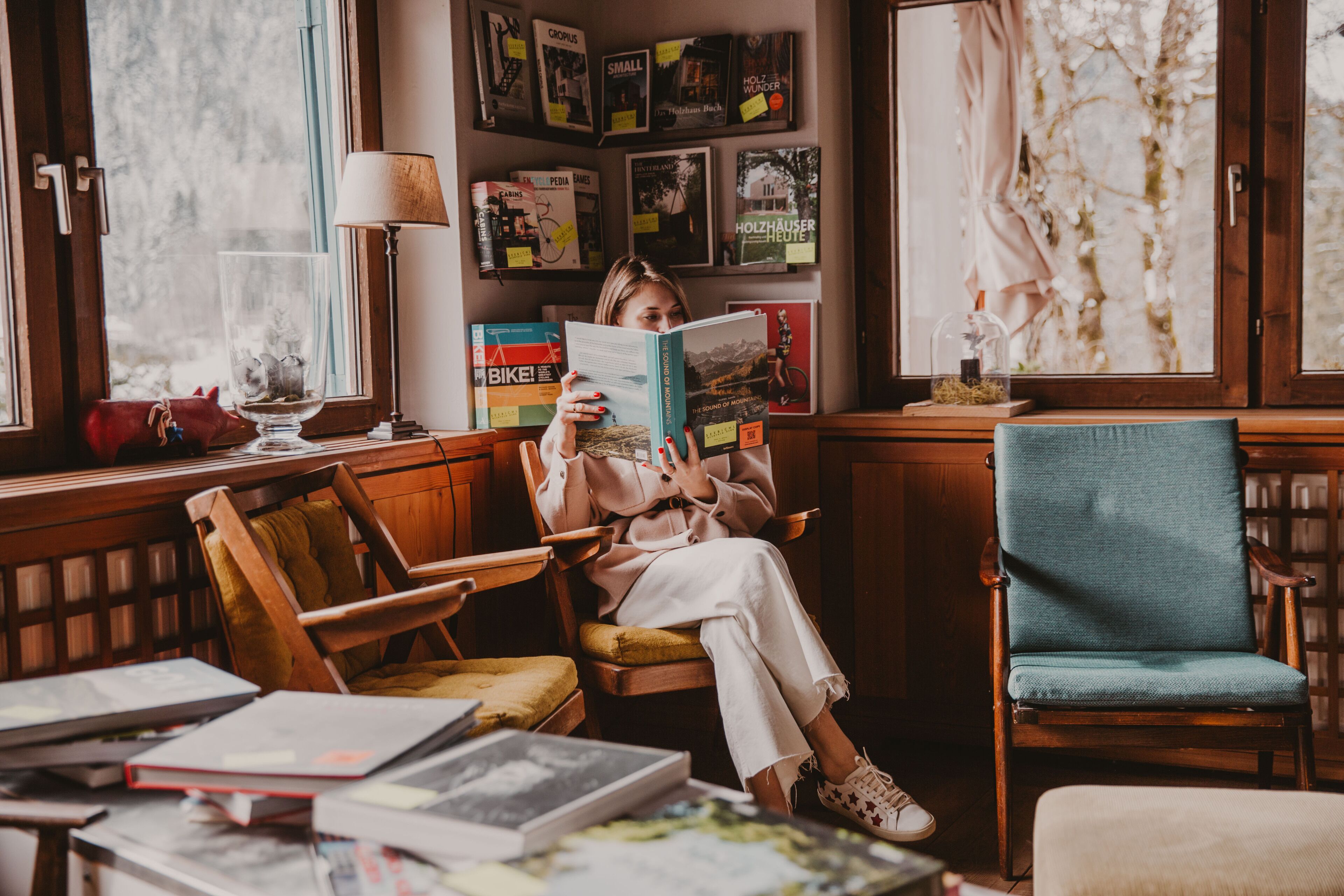 A cozy reading nook with a person reading a book, surrounded by bookshelves and a window with a view.