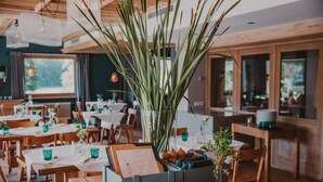 En restaurant med træborde og -stole, en stor potteplante og udsigt til det fri.
