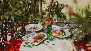 An outdoor dining table with plates of food, a green glass, and a terracotta pot.