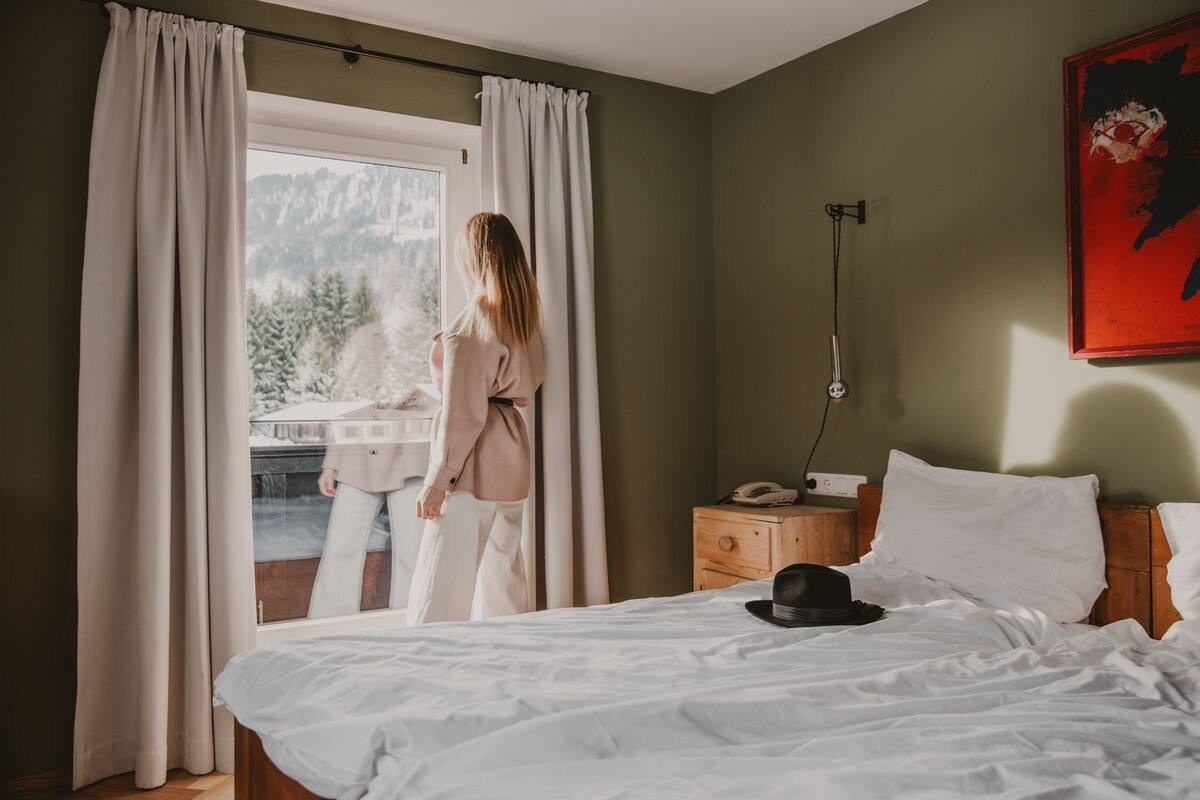 Un dormitorio con cama, mesita de noche, teléfono y ventana con cortinas.