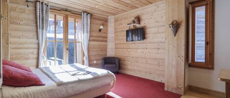 Dormitorio con paneles de madera, una cama, alfombra roja y una ventana con cortinas.