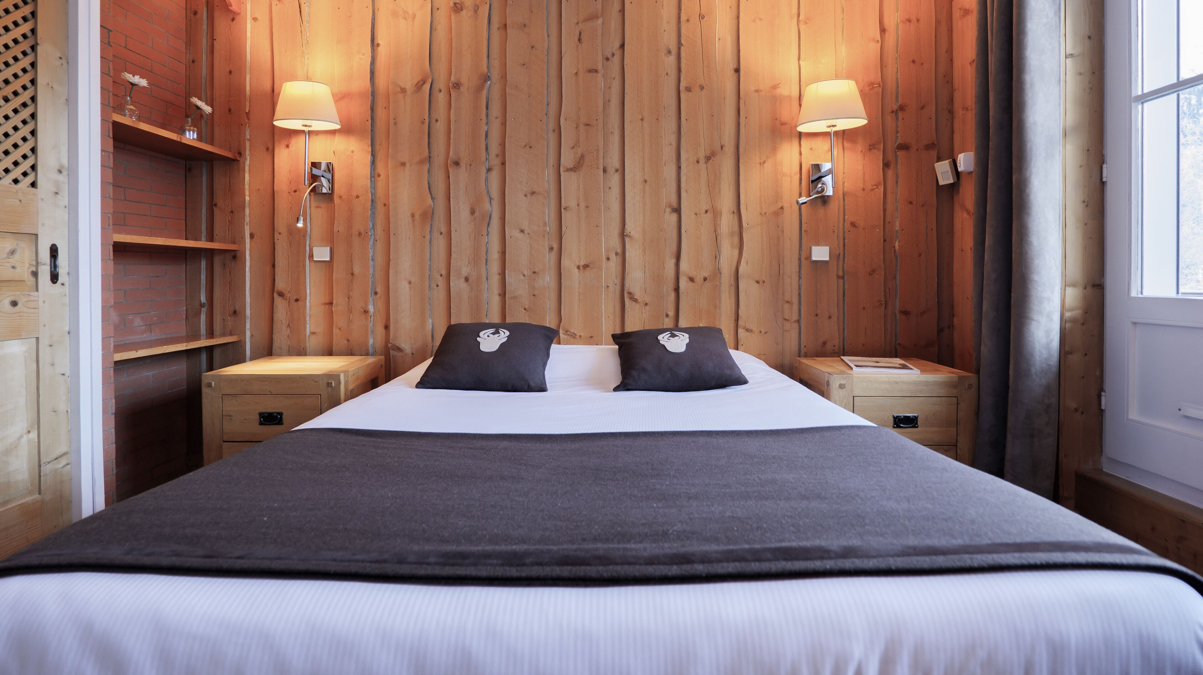 A wooden-paneled room with a bed, two bedside tables, and wall-mounted lamps.