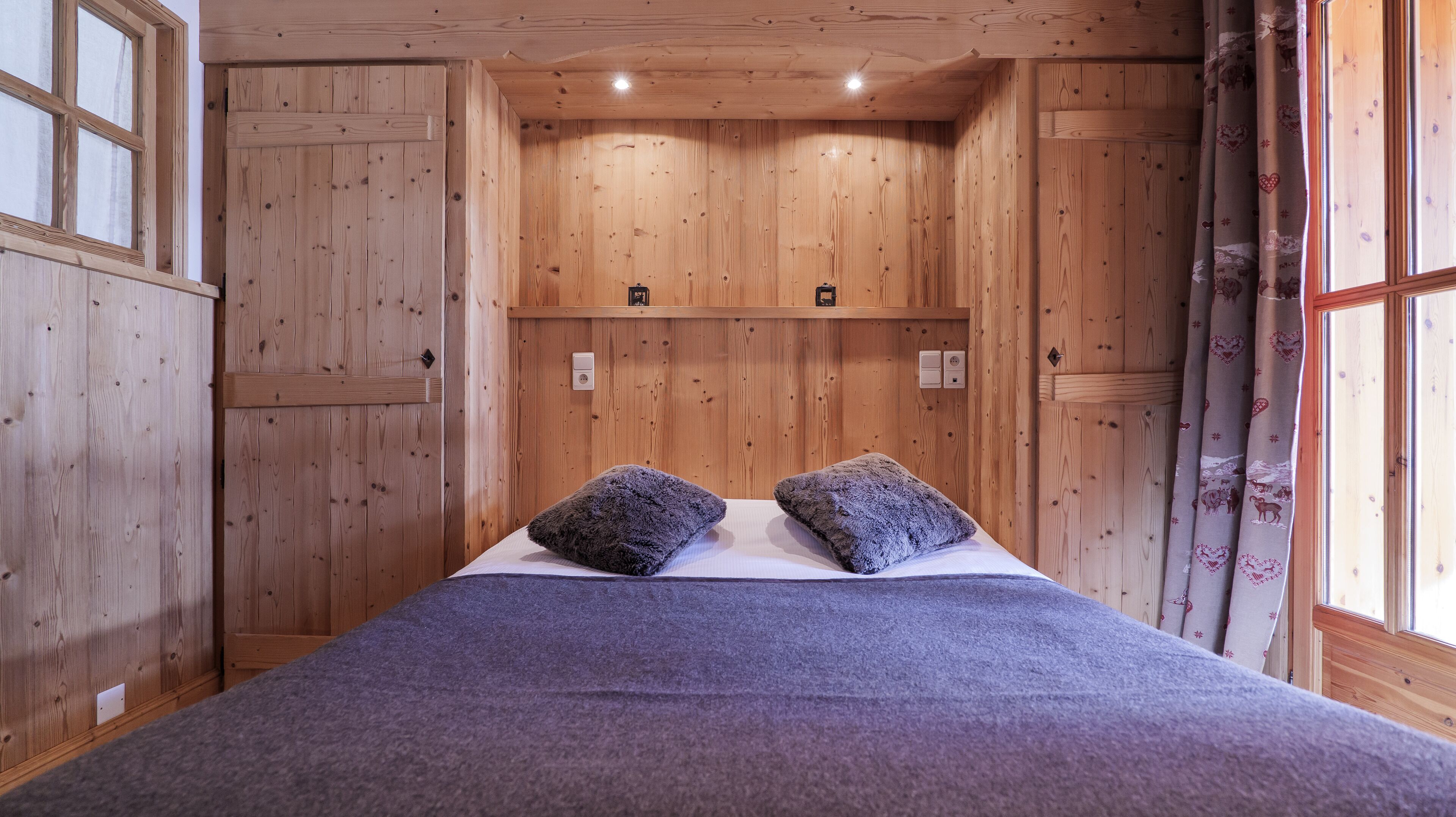 Une pièce en bois avec un lit, deux oreillers et une fenêtre avec des rideaux.