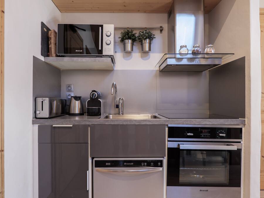 A compact kitchen with a toaster, kettle, sink, and Brandt appliances.