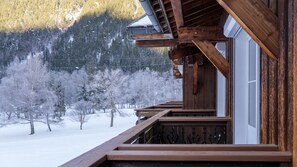A wooden cabin with a balcony overlooking a snowy landscape and trees.