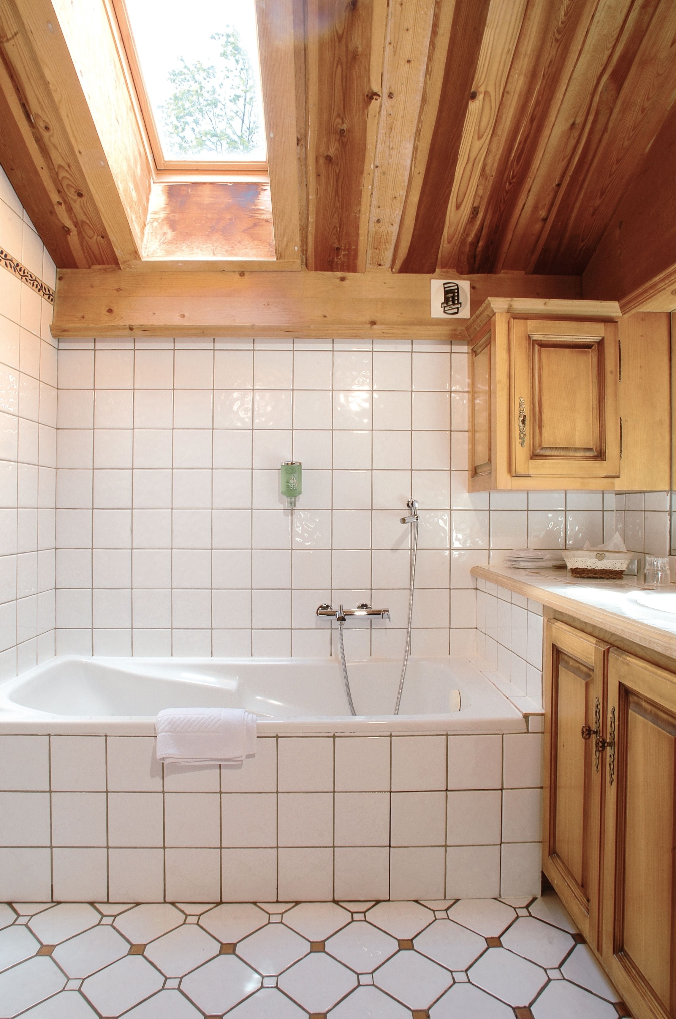 Un baño con bañera, tragaluz, paredes de azulejos y armarios de madera.