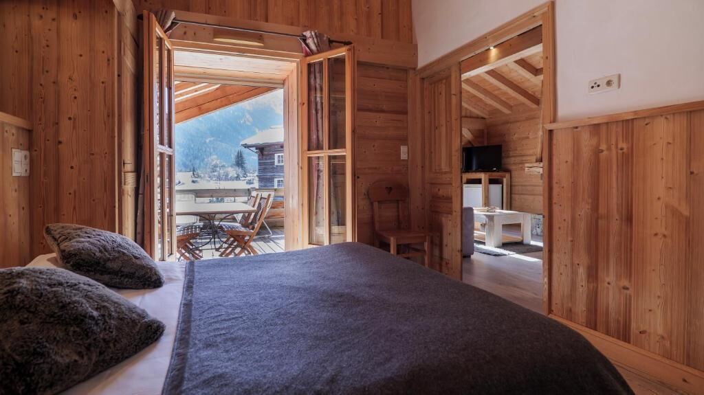 A wooden room with a bed, a television, and a view of a mountain.