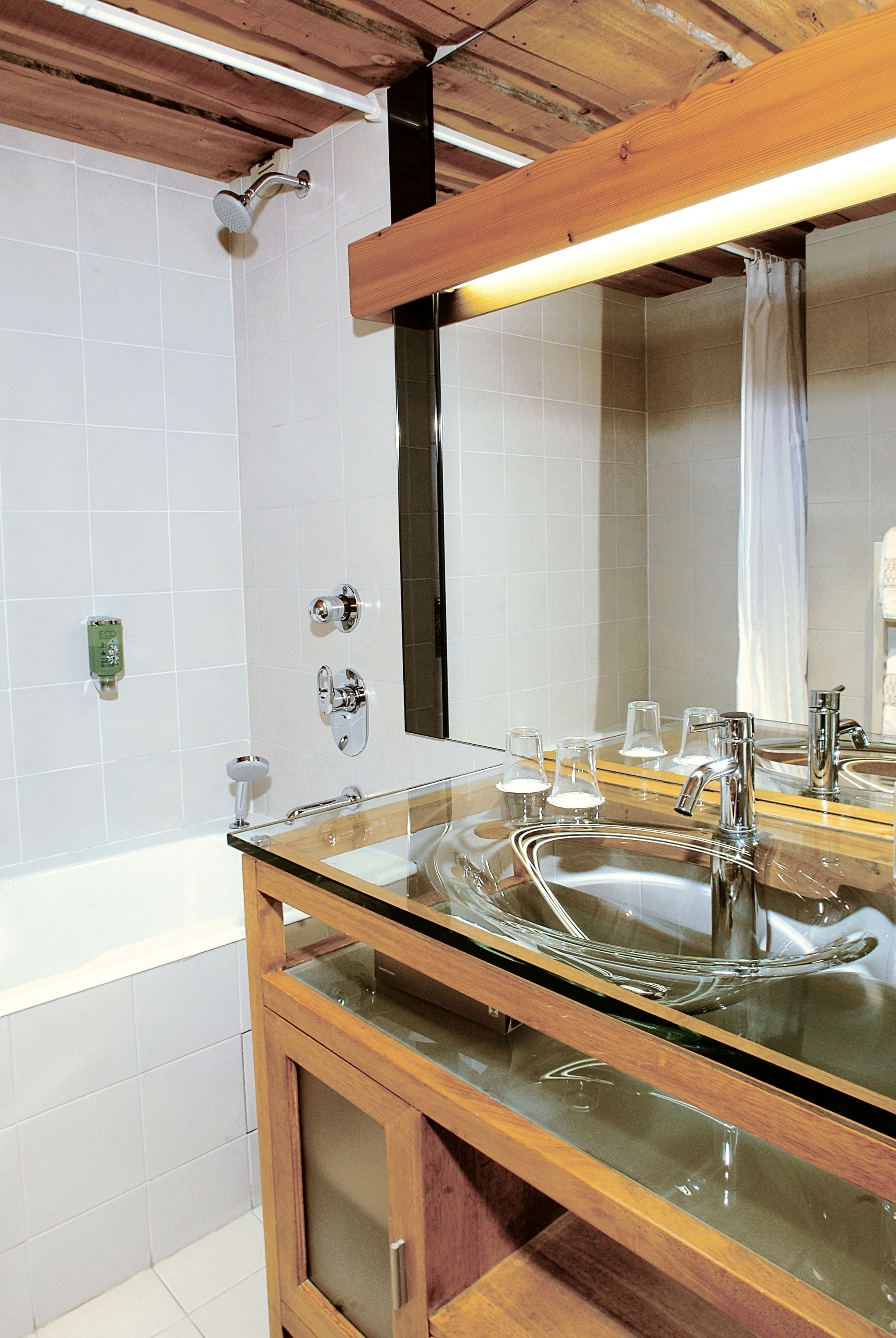 Ein Badezimmer mit einem Glaskonstruktion-Waschbecken, einer Dusche und einer Holzbalkendecke.