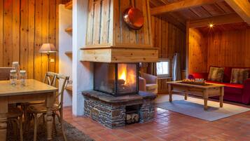 A cozy log cabin interior with a stone fireplace, wooden walls, a dining area, and a red sofa.