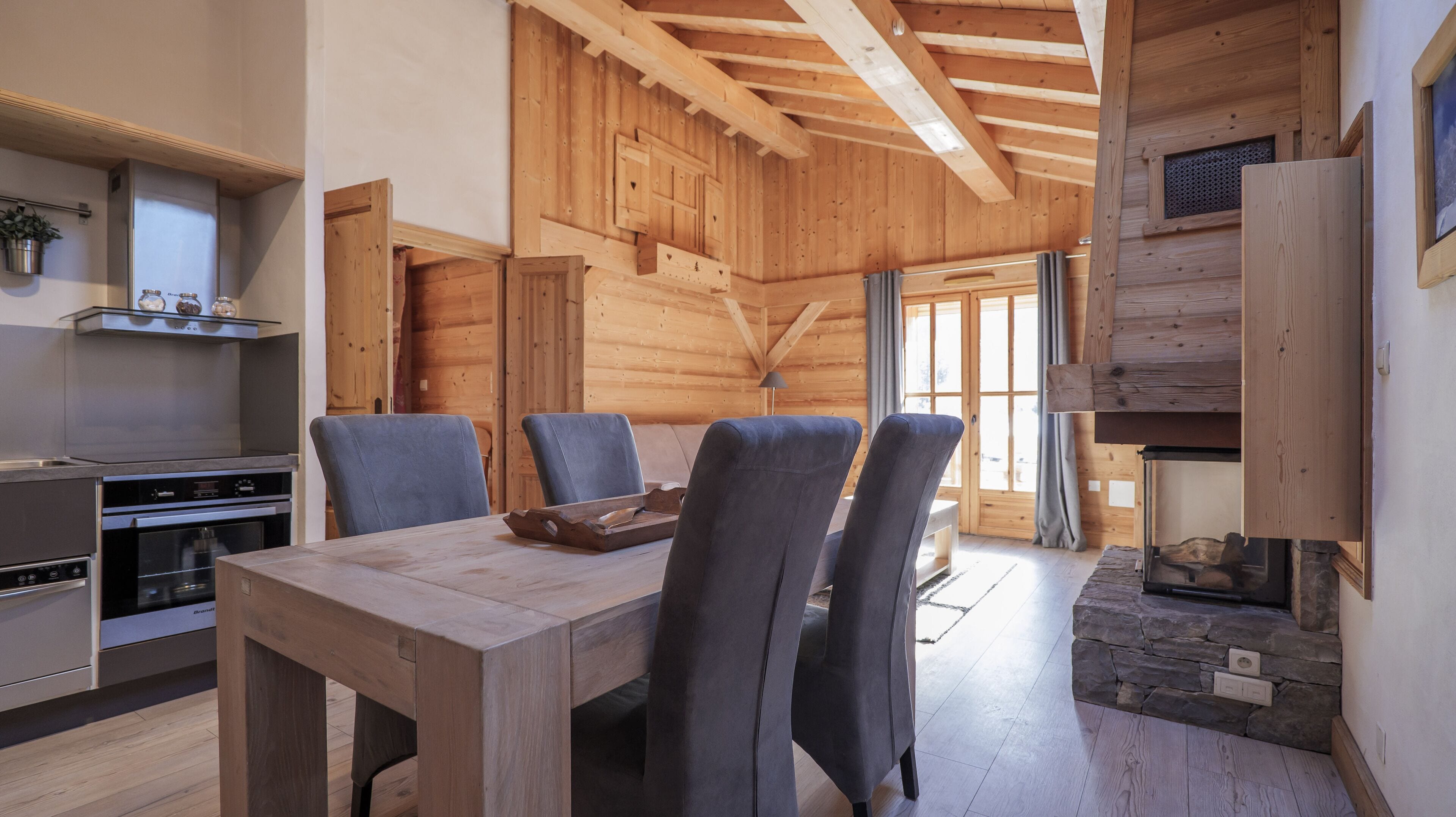 A wooden interior with a dining table, chairs, a kitchen area, and a stone fireplace.