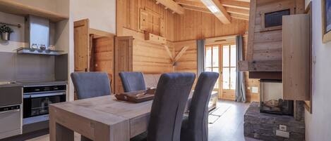 A wooden interior with a dining table, chairs, a kitchen area, and a stone fireplace.