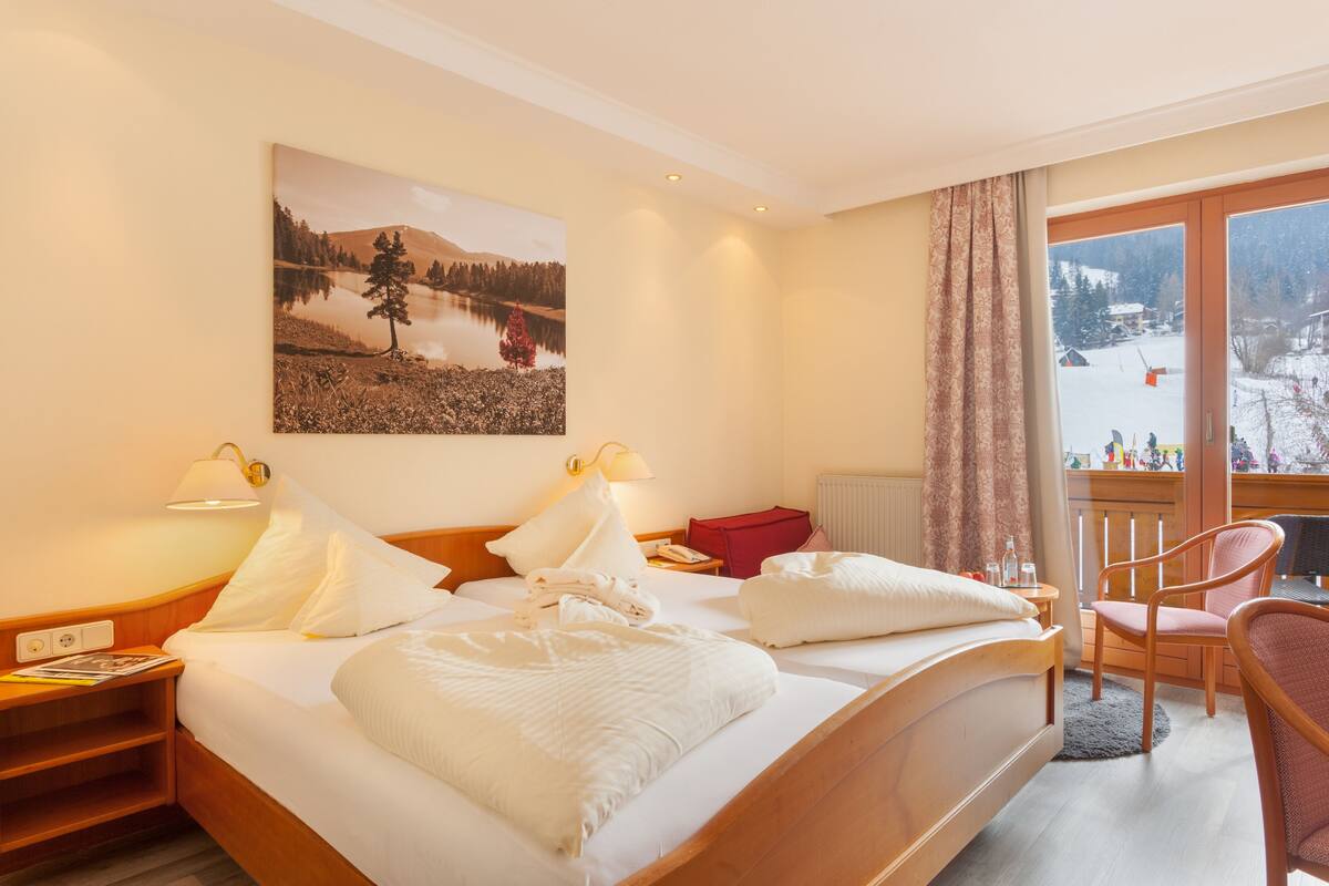 Une chambre d’hôtel avec un grand lit, deux tables de chevet, une chaise, un bureau et une fenêtre donnant sur un paysage enneigé.
