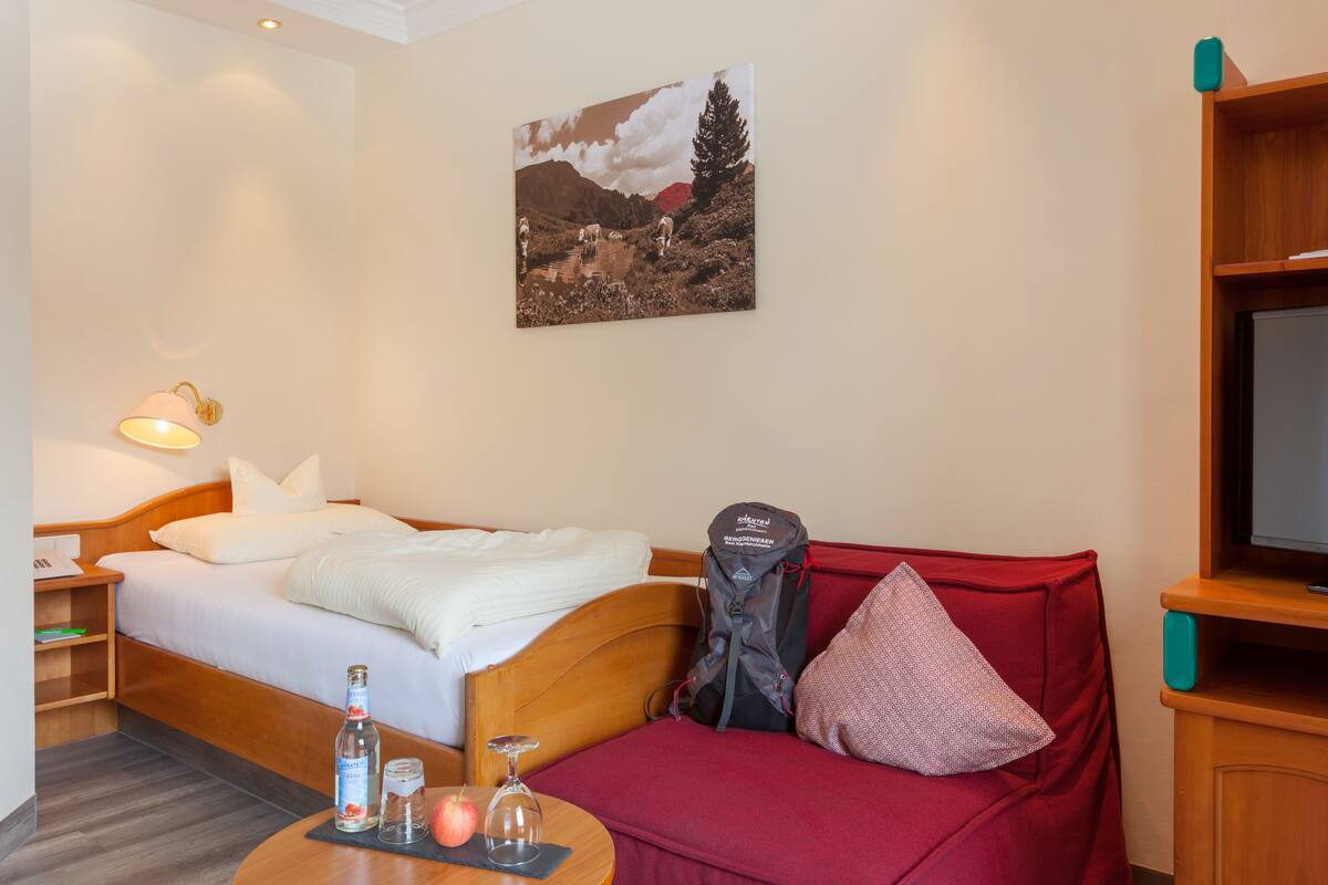 Une chambre d’hôtel avec un lit, un canapé rouge, une table avec une bouteille et un verre, une télévision et un tableau au mur.