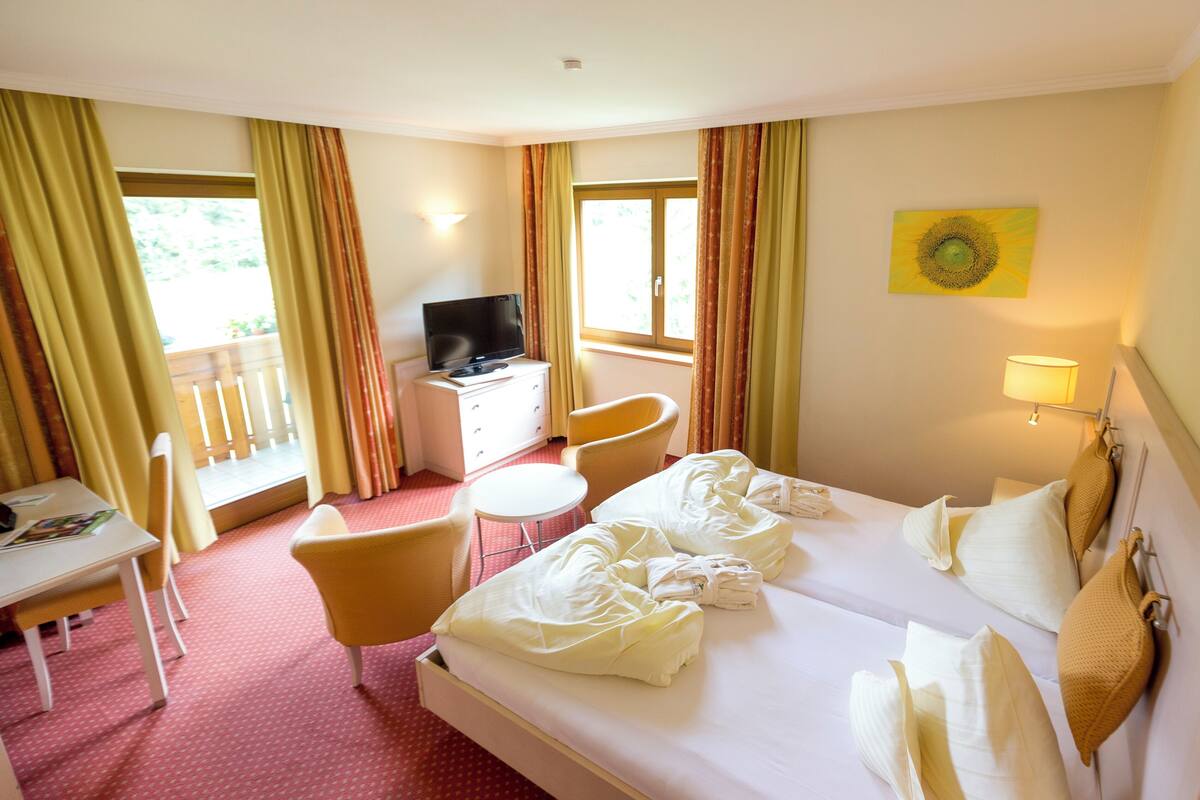 Une chambre d’hôtel avec un lit, deux chaises, un bureau, une télévision et une fenêtre avec des rideaux.
