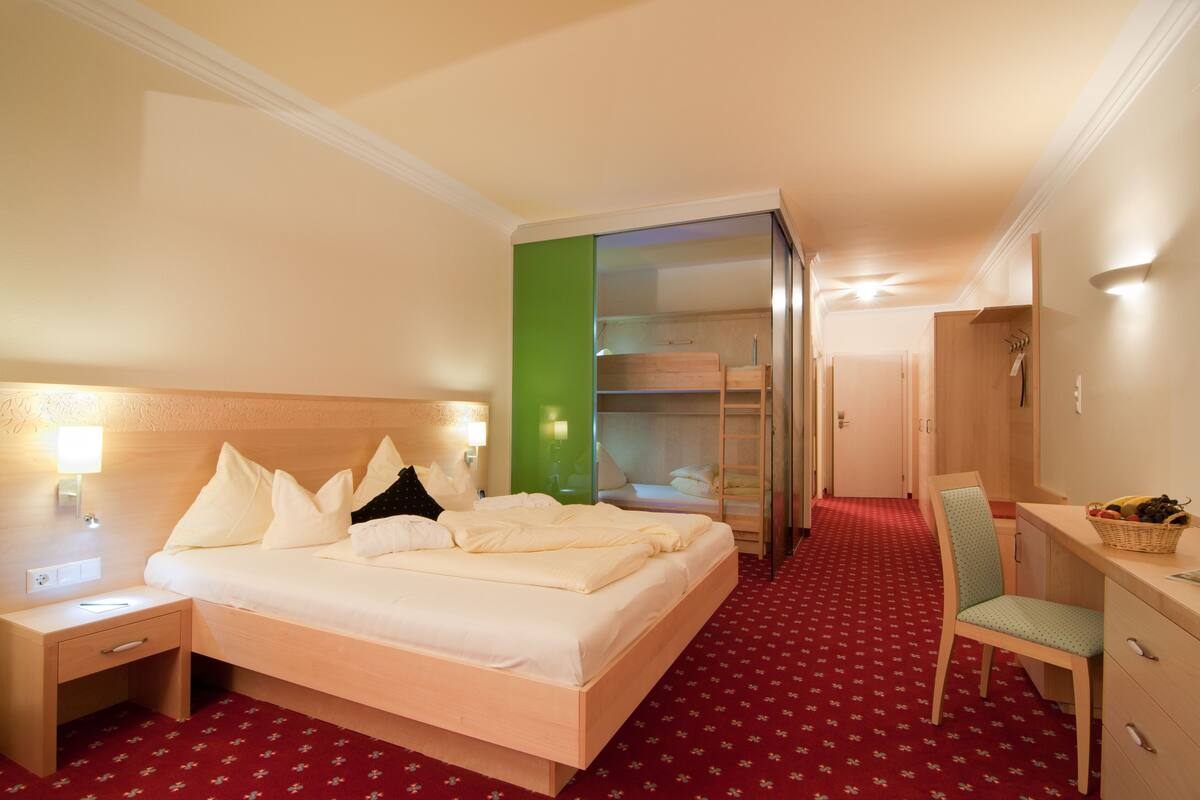 Une chambre d’hôtel comprenant un lit, un bureau, une chaise, une armoire et une salle de bain visible à travers une porte en verre.